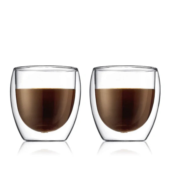 Two clear glass cups filled with a dark liquid on a white background