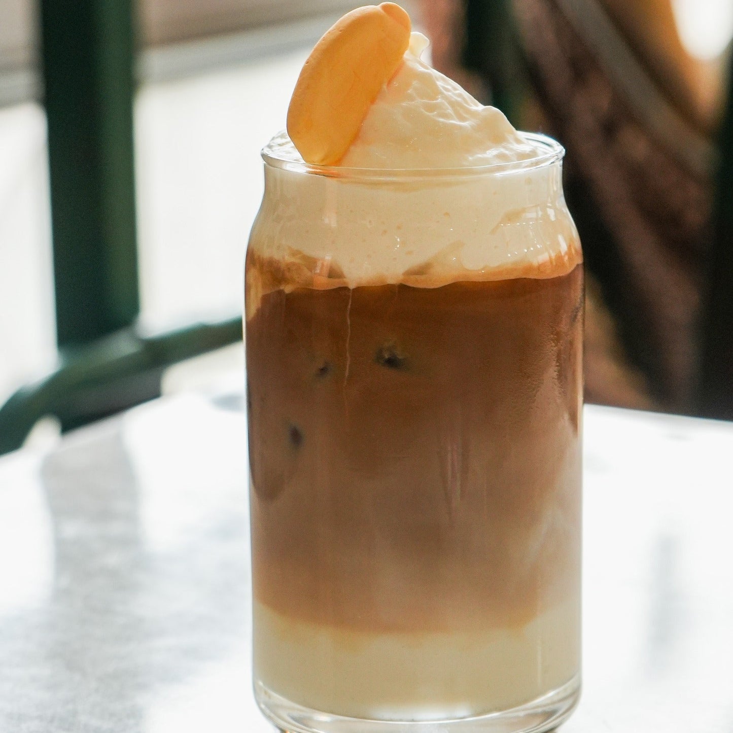 Layered iced coffee with whipped cream and a orange slice on a glass in a cafe setting.
