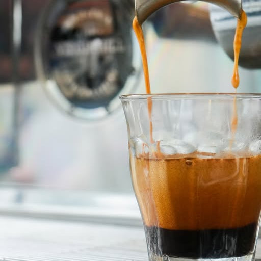 Espresso being poured into a glass with ice cubes, blurred background