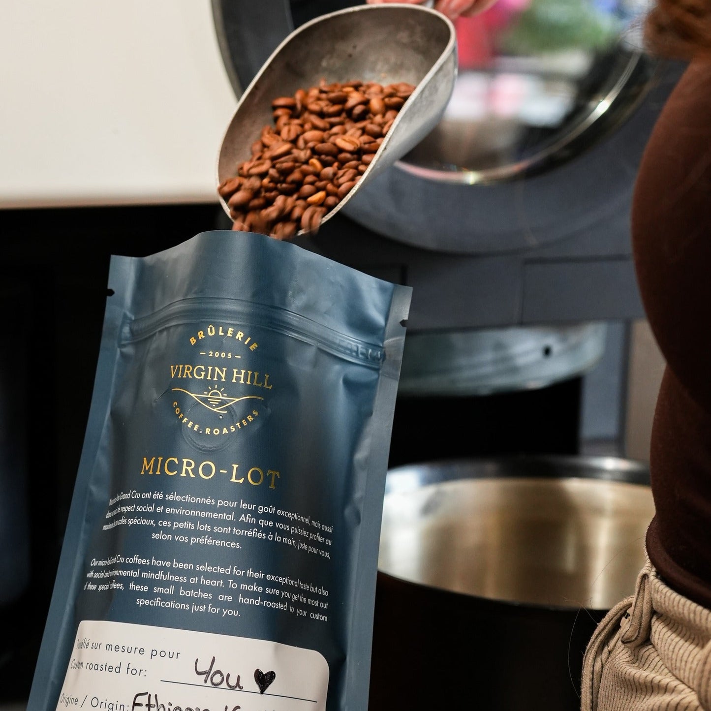 Coffee beans being poured from a scoop into a blue Virgin Hill coffee bag.