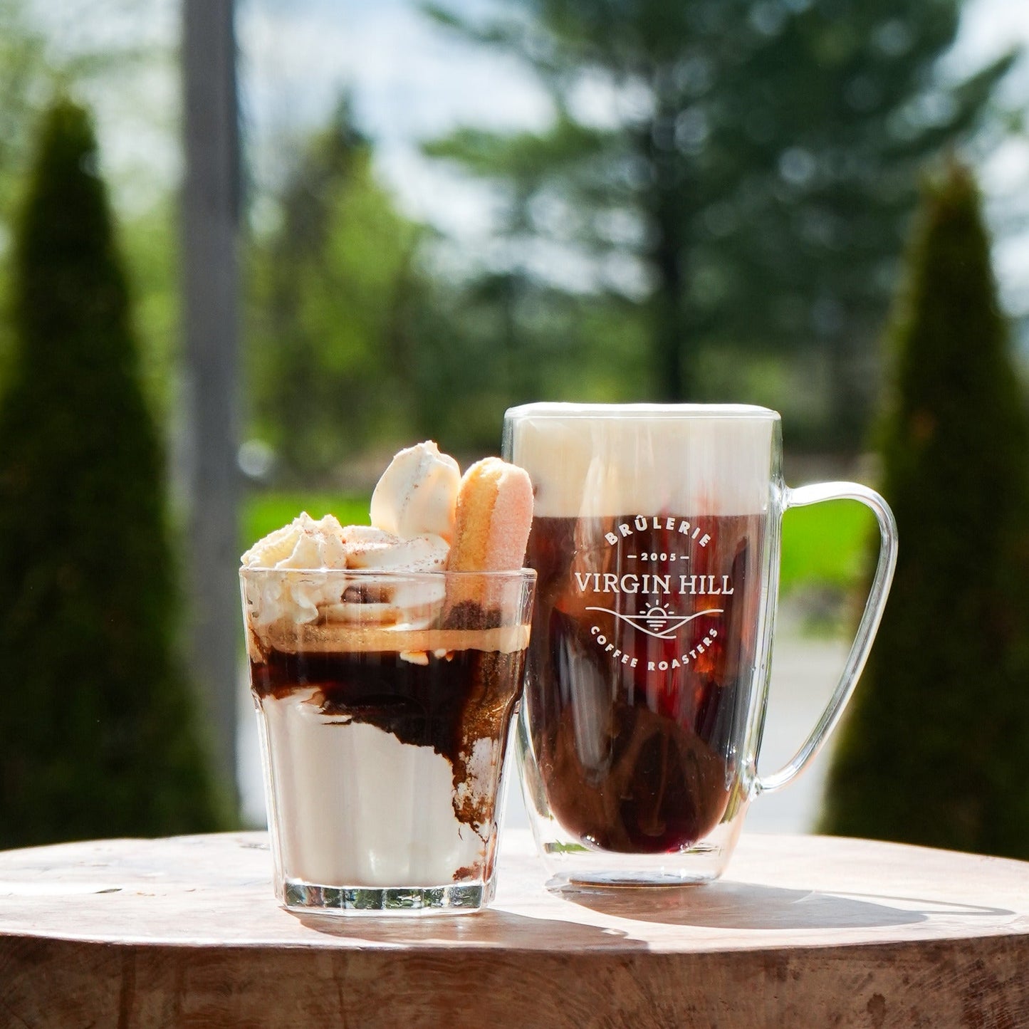 Two glasses of iced coffee on a wooden surface with a blurred natural background