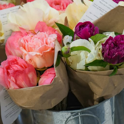 Bouquets of pink, white, and purple flowers wrapped in brown paper on a metal surface.