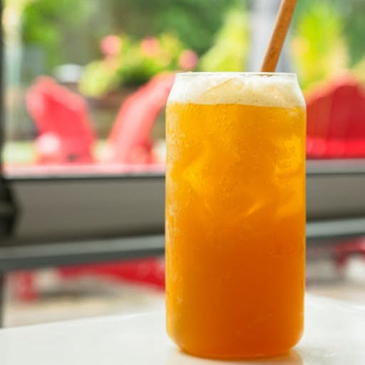 Glass of goldne chai with a straw on a blurred outdoor background