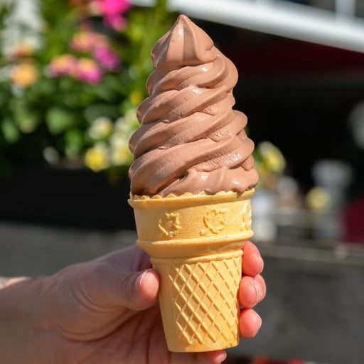 Chocolate ice cream cone held by a hand with a blurred outdoor background