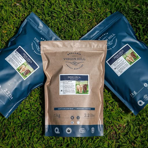Three bags of Virgin Hill Organic Grass-fed Beef Bone Meal dog food arranged on green grass, with one central kraft paper bag and two blue bags flanking it.