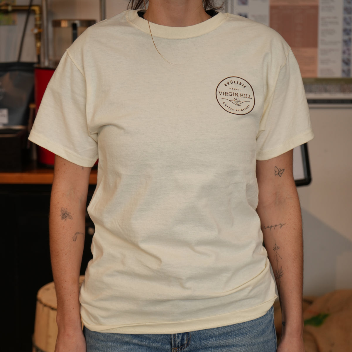Person wearing a beige t-shirt with a logo in an indoor setting