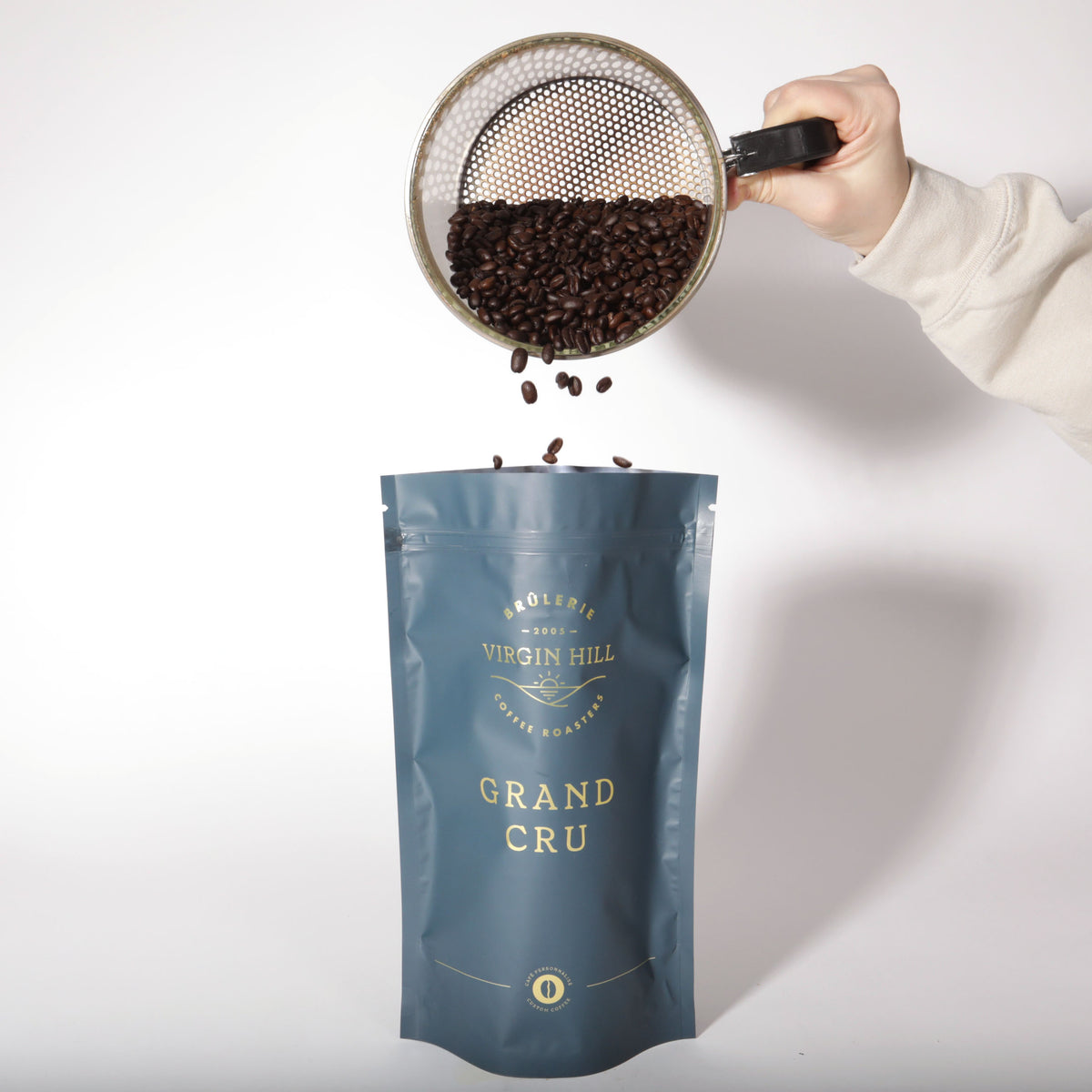 Hand pouring coffee beans from VH into a 'Grand Cru' coffee bag on a white background