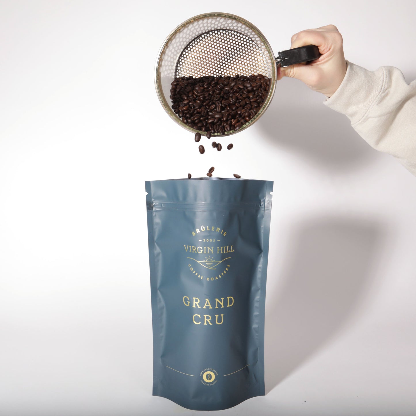 Hand pouring coffee beans from VH into a 'Grand Cru' coffee bag on a white background