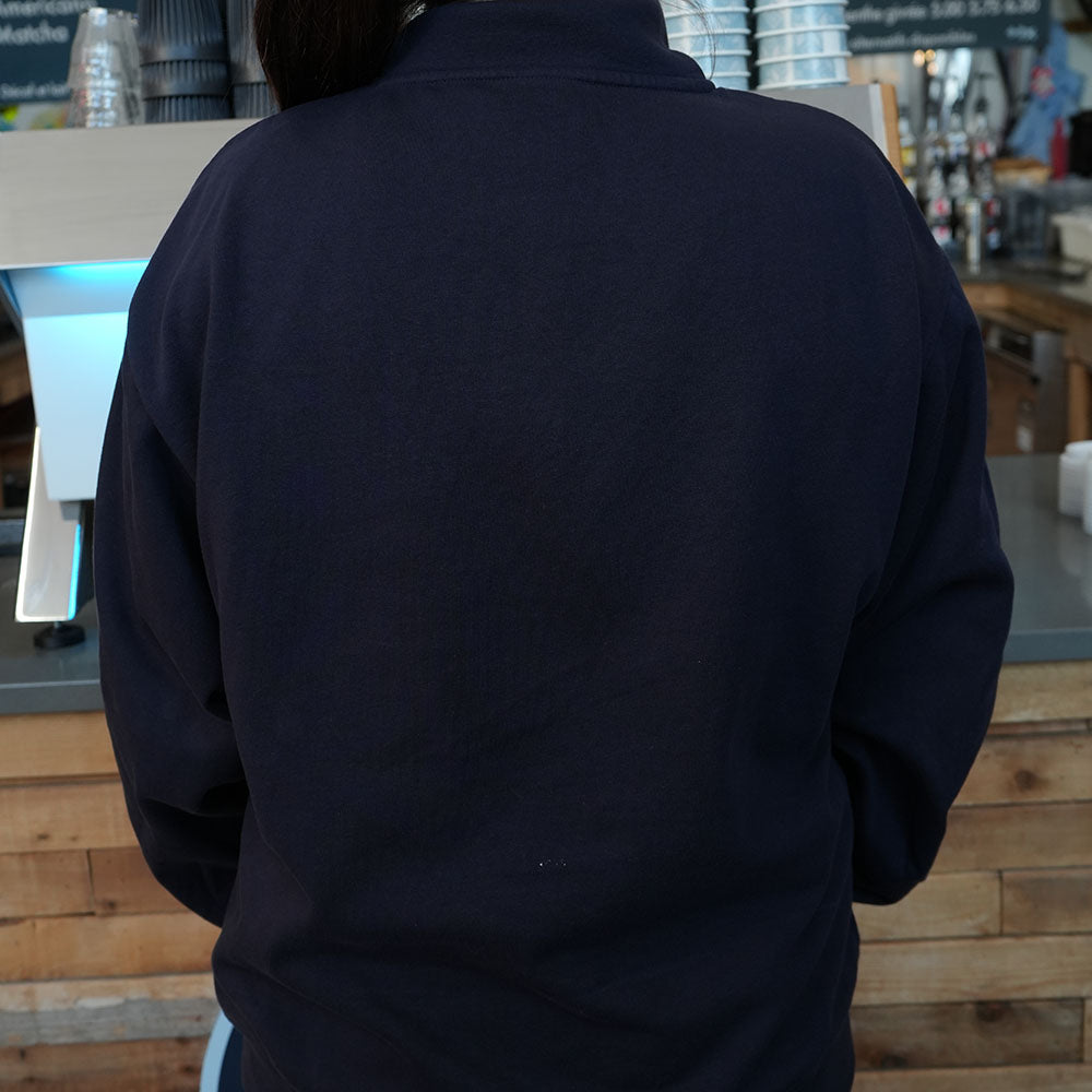 Person wearing a dark blue jacket in an indoor setting with wooden elements.