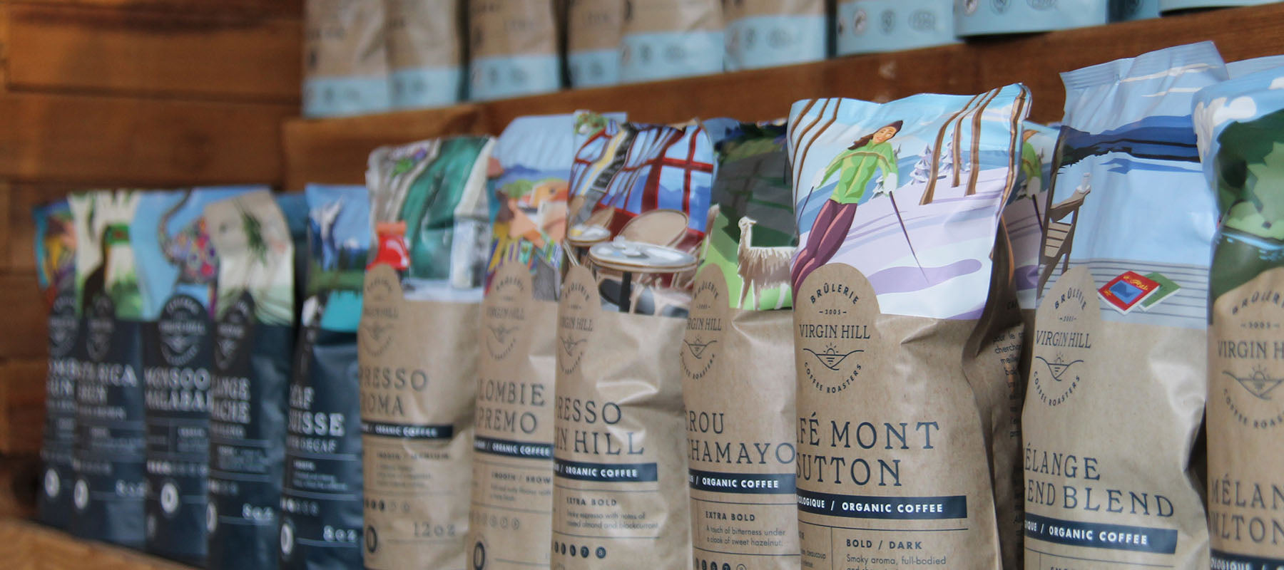Row of coffee bags with various designs and branding on a wooden shelf.