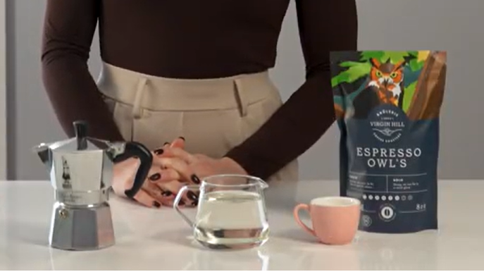 Woman standing behind a table with coffee-making equipment and coffee beans.