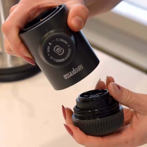 Person holding a black coffee grinder with 'OXO' branding on a kitchen counter.