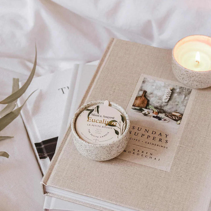 Small round container labeled 'Eucalyptus' on top of a book with a lit candle beside it.